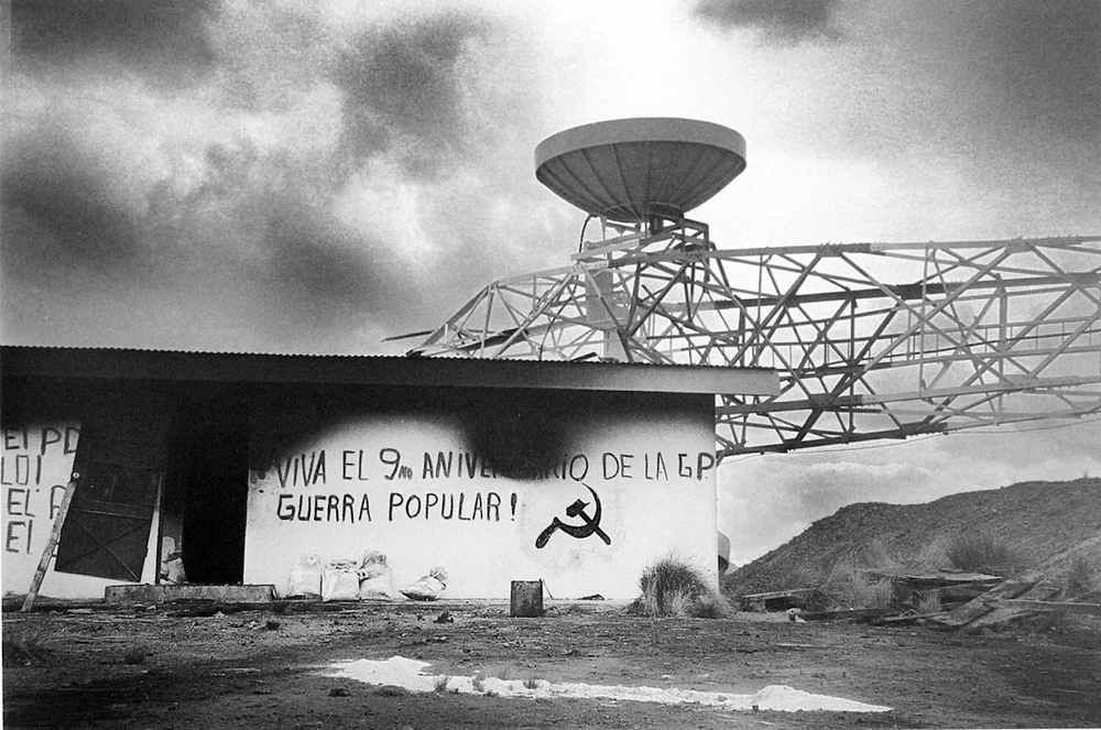 Grafitti on a building next to a destroyed communications tower, 'LONG LIVE THE 9th ANNIVERSARY OF THE P.W. PEOPLE'S WAR!'